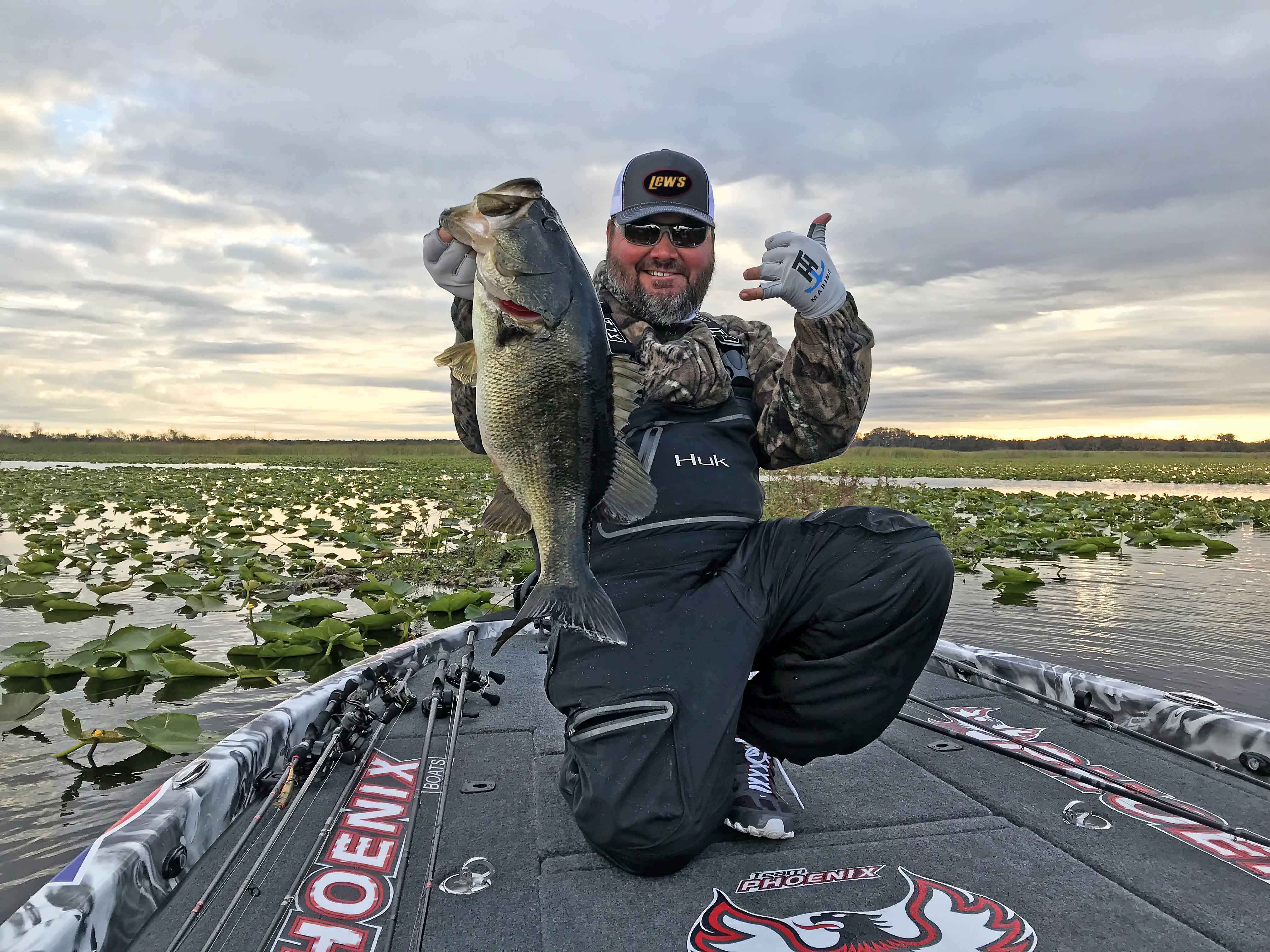 Greg Hackney holding out a bass caught from the surrounding lily pad cover